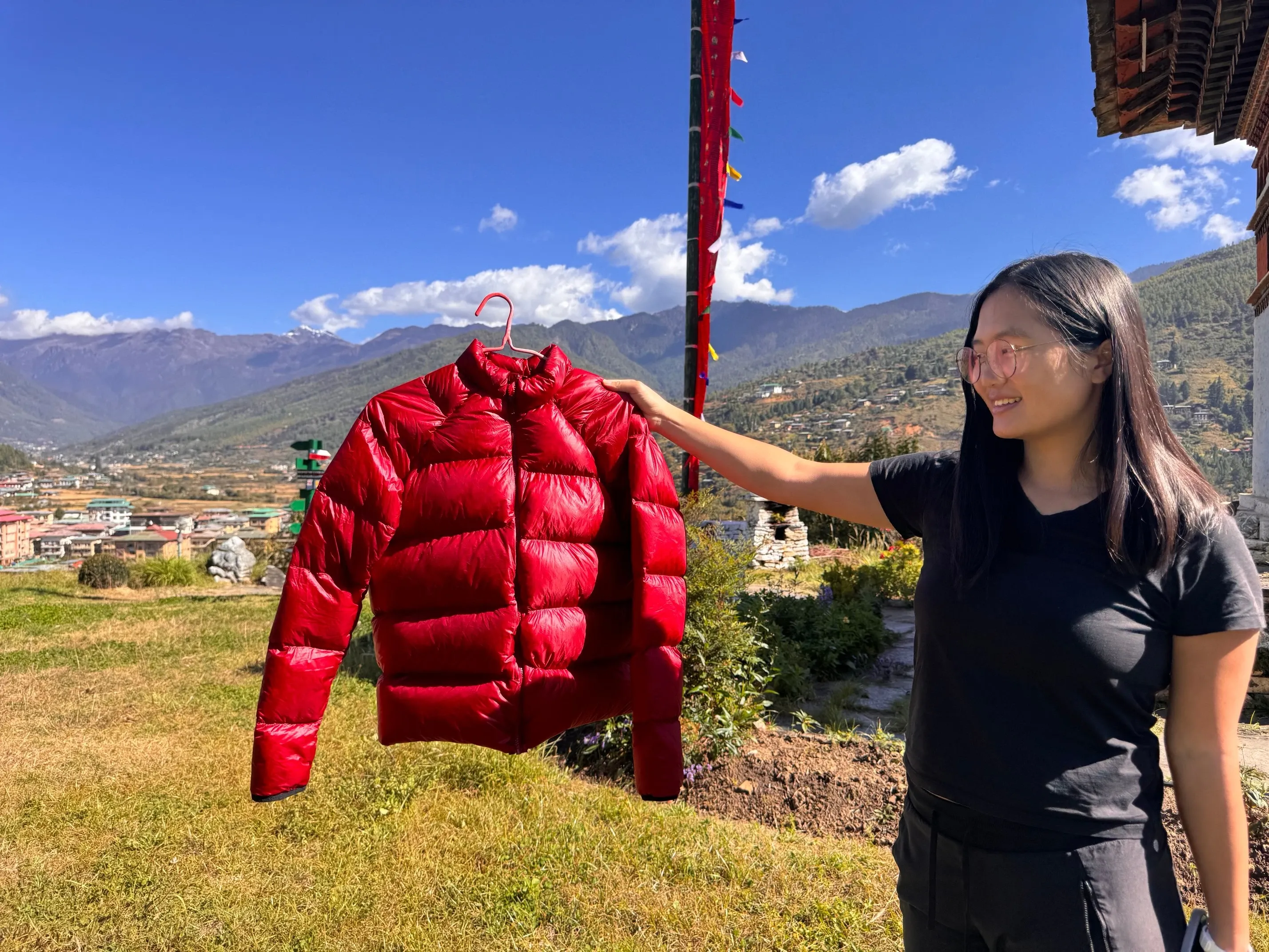 holding a red puffy jacket against a backdrop with mountains and a stupa