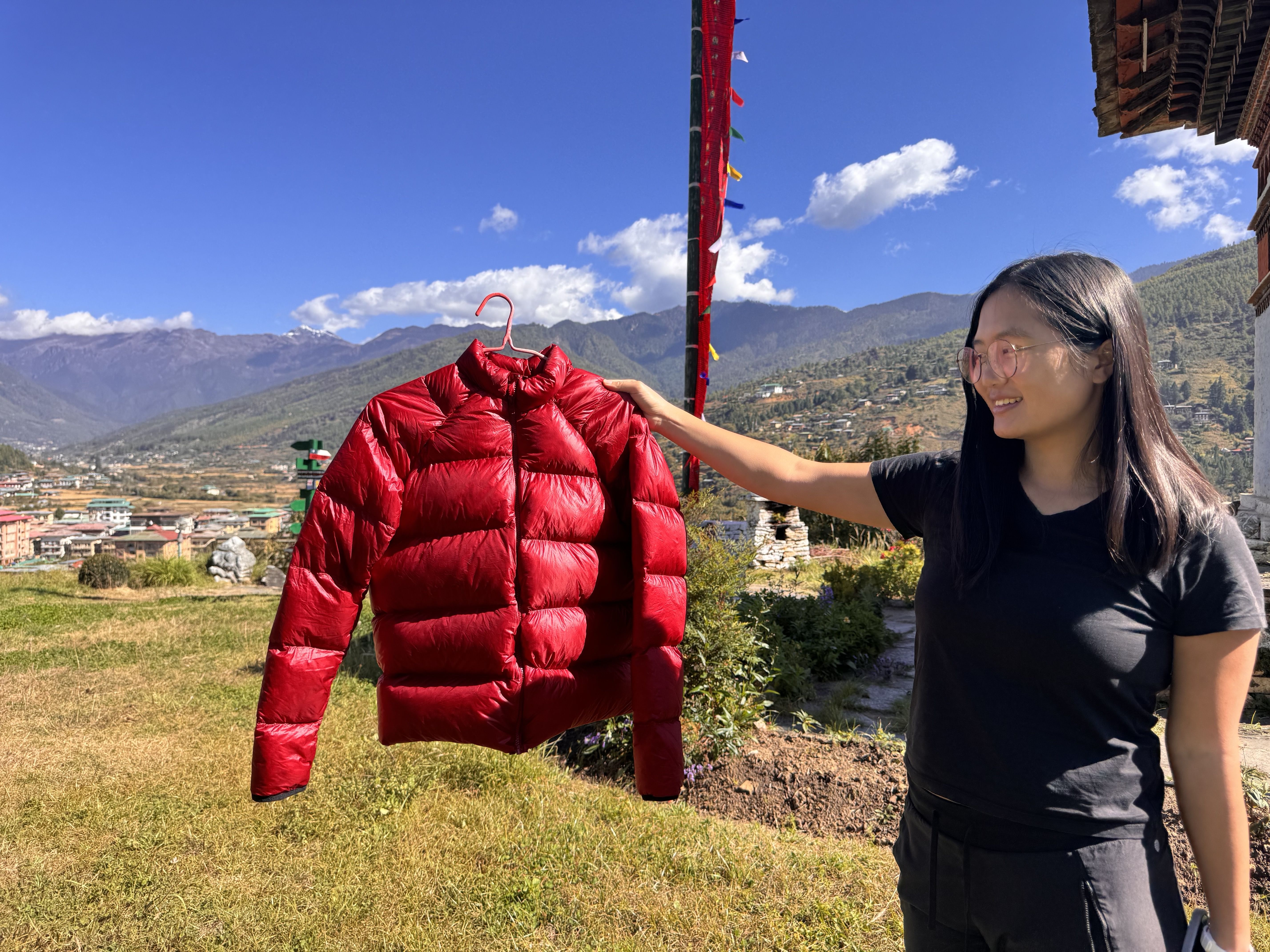 holding a red puffy jacket against a backdrop with mountains and a stupa